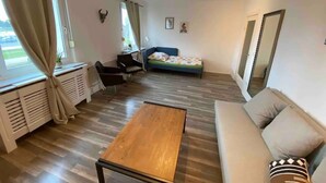 Ein Zimmer mit einem Bett, einer Couch, einem Holztisch, einem Sessel, einer Heizung und einem Fenster mit Vorhängen.