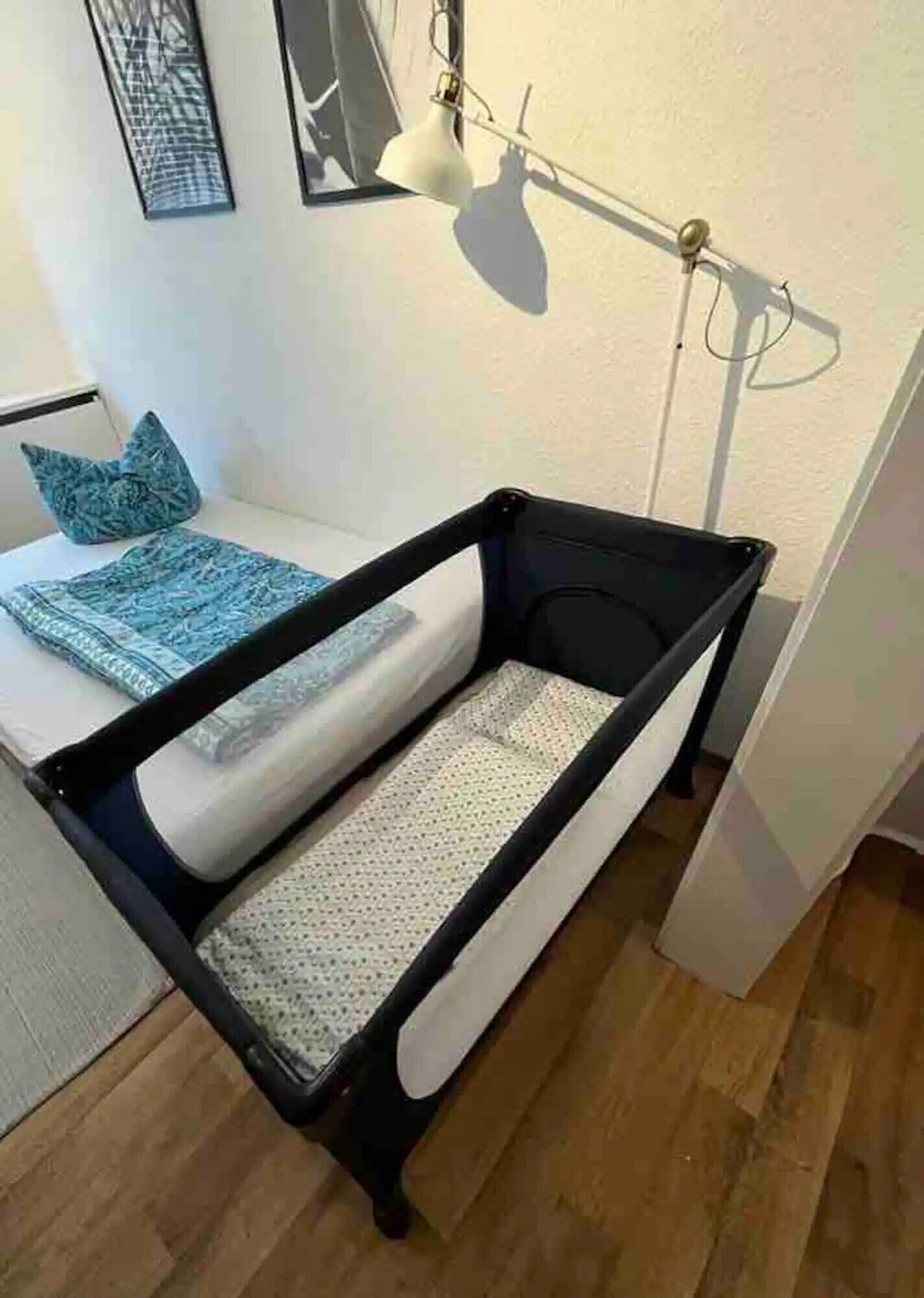 Een kamer met een ledikantje, een wandlamp en een lijst met een afbeelding.