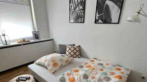 Ein kleines, modernes Schlafzimmer mit einem Bett, einem kleinen Tisch und einem Fenster mit Jalousien.