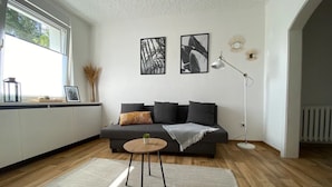 Ein modernes Wohnzimmer mit einem grauen Sofa, einem kleinen runden Tisch und einer Stehlampe.