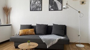 Ein modernes Wohnzimmer mit einem grauen Sofa, einem kleinen runden Holztisch und einer Stehlampe.