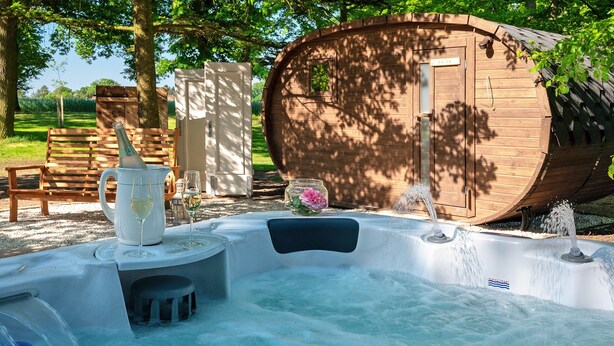 Un jacuzzi con estructura de barril de madera, un banco de madera y una mesa con una jarrón y vasos.