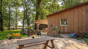 Una cabaña de madera con mesa de picnic, arena y juguetes de exterior.