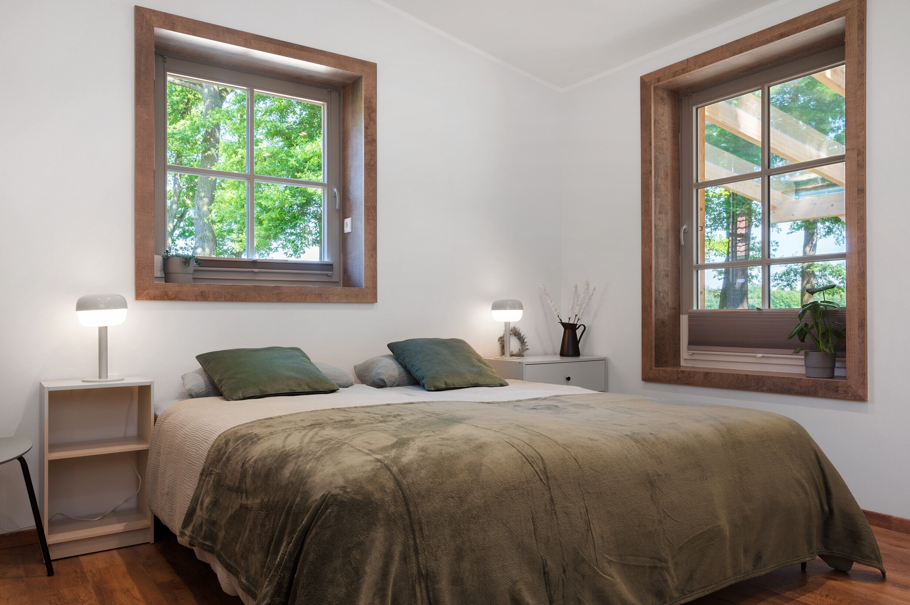 Ein Schlafzimmer mit einem Bett, zwei Nachttischen, zwei Fenstern und einem Beistelltisch.