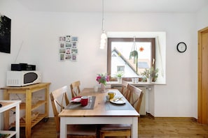 A dining area with a wooden table, chairs, a microwave, and a window with a view of a house and plants. - Apartment 'Ferienwohnung Lilly' with Private Terrace and Wi-Fi (Eitelborn)