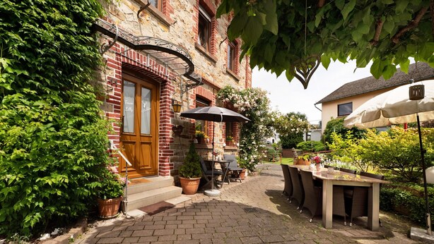 Un bâtiment en briques avec une porte en bois, des places assises à l’extérieur et des plantes en pot.