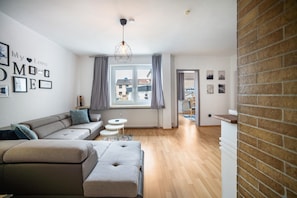 Een moderne woonkamer met een hoekbank, een voetenbankje en een eethoek met een kleine tafel en stoelen.