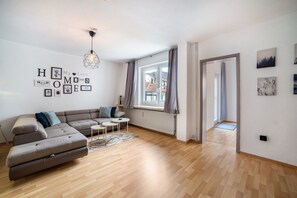 Een moderne woonkamer met een hoekbank, een klein rond tafeltje en een hanglamp.