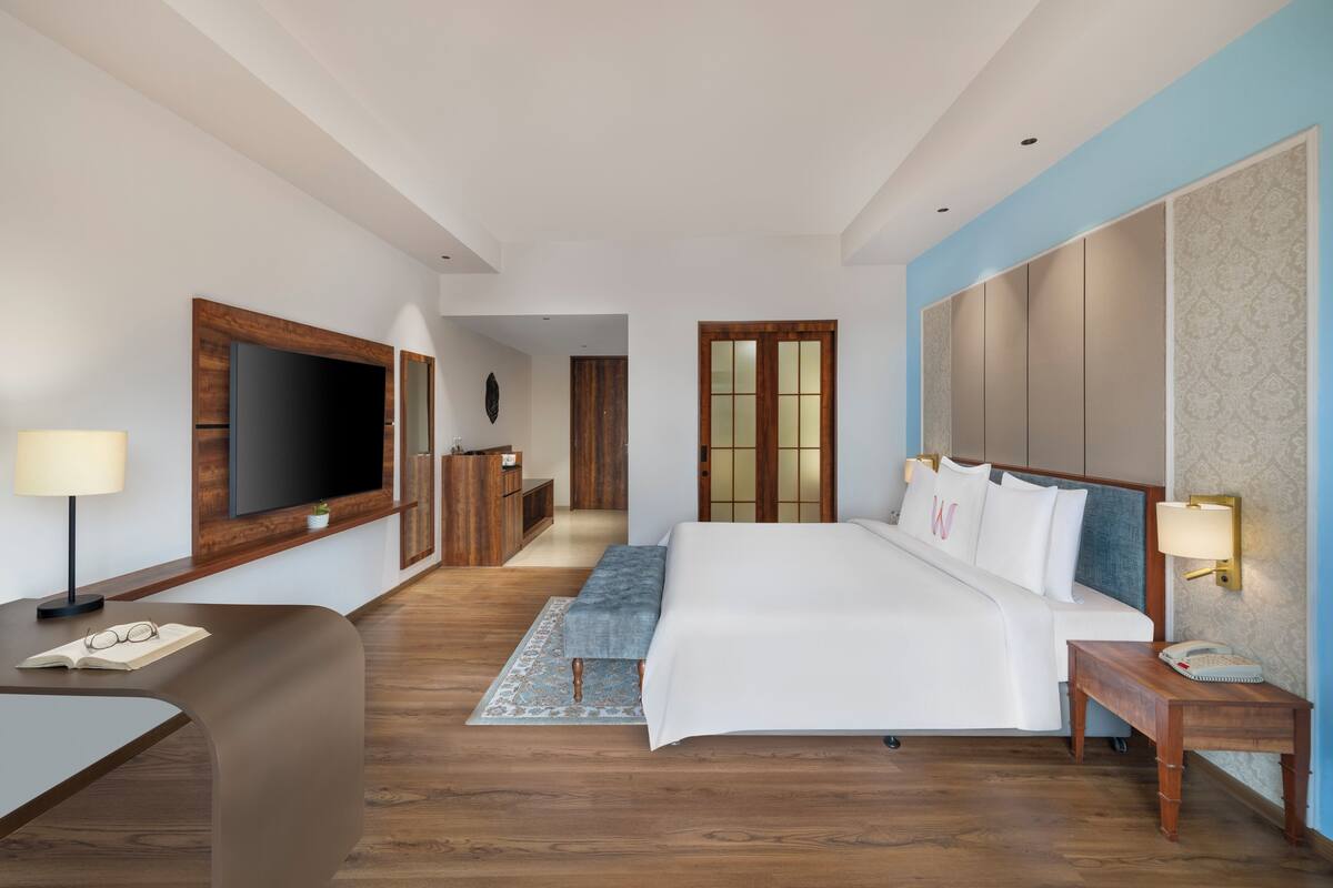 Una habitación de hotel moderna con una cama grande, un escritorio con lámpara, un televisor y un armario.