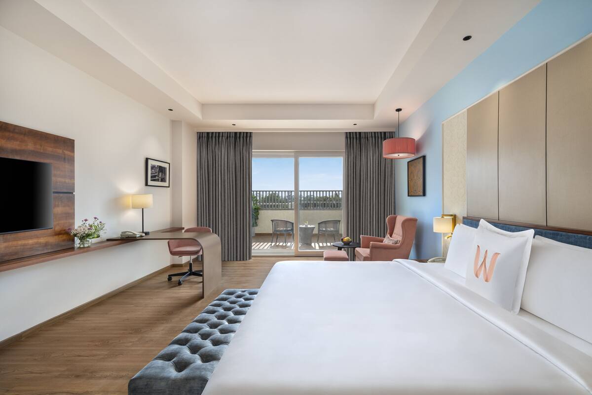Habitación de hotel con una cama grande, un escritorio, una silla, un televisor y un balcón con vistas.