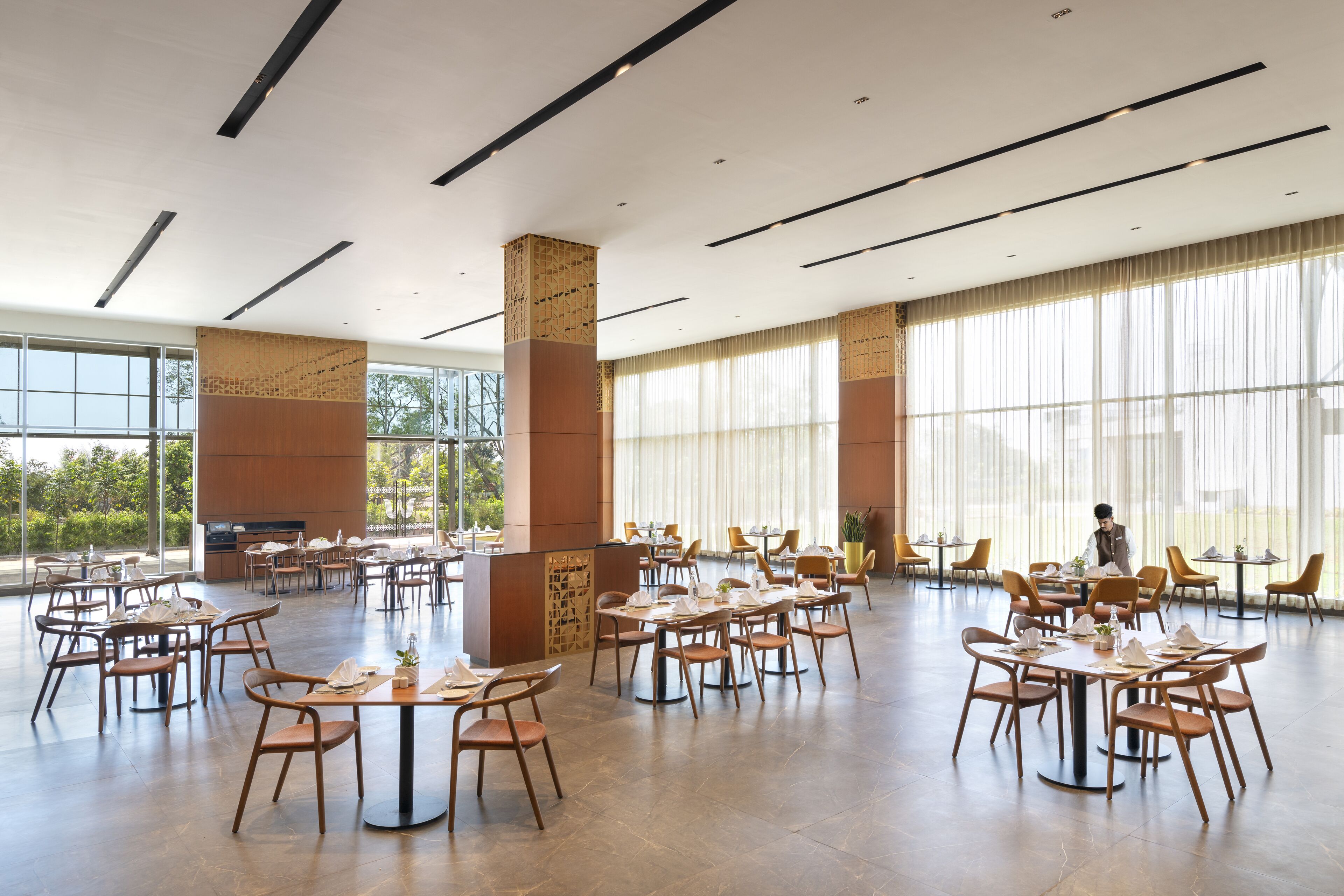 Een ruime eetruimte met meerdere tafels en stoelen, grote ramen en een modern plafondontwerp.