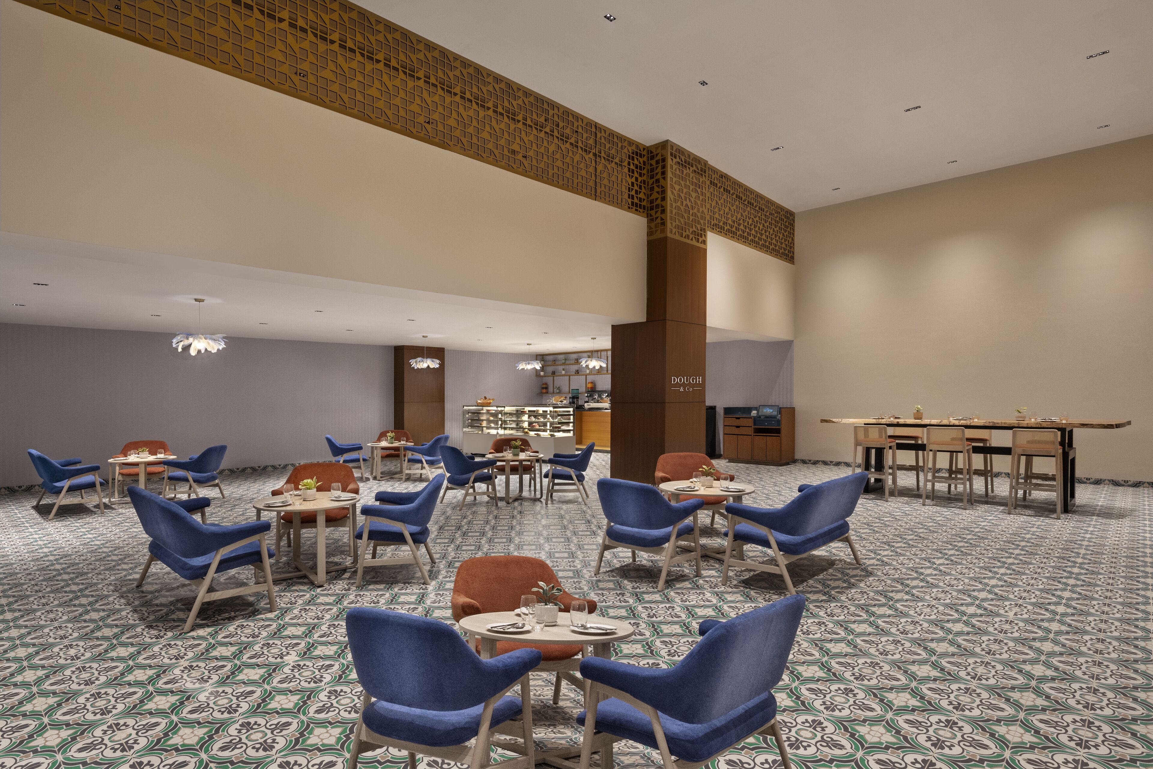Un vaste espace dédié à la salle à manger, avec des chaises bleues et des tables rondes, un sol à motifs et un plafond haut orné d’un panneau décoratif en bois.
