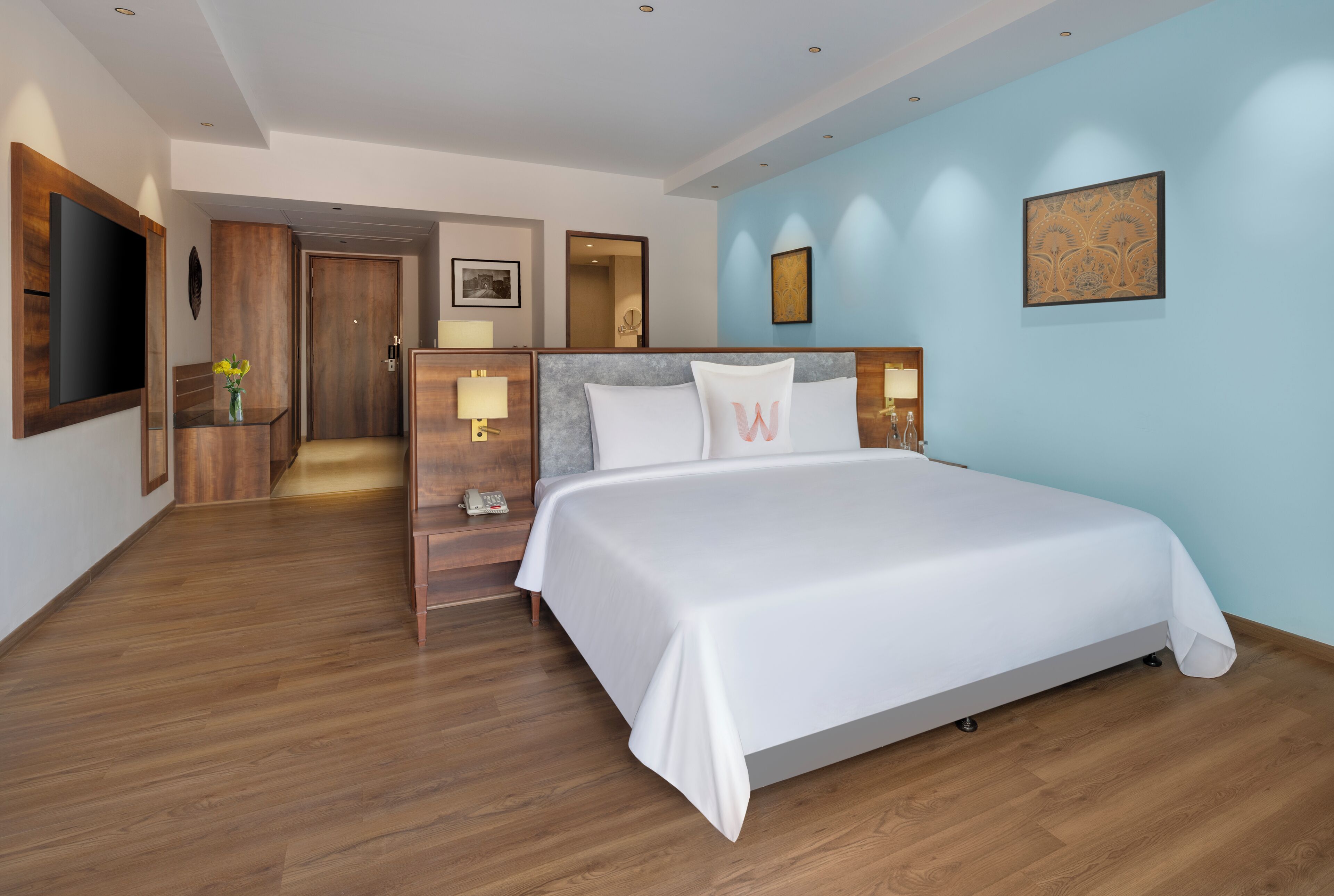 Une chambre d’hôtel moderne avec un grand lit, un plancher en bois, une télévision, un bureau avec une lampe et une petite plante.