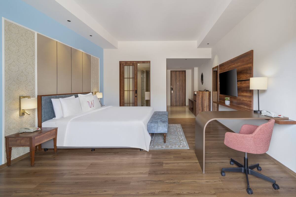 Una habitación de hotel moderna con una cama grande, un escritorio con una silla, un televisor y un espejo.