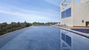 A clear blue infinity pool with a modern building and palm trees in the background. - Welcomhotel By ITC Hotels Belagavi (Belagavi)