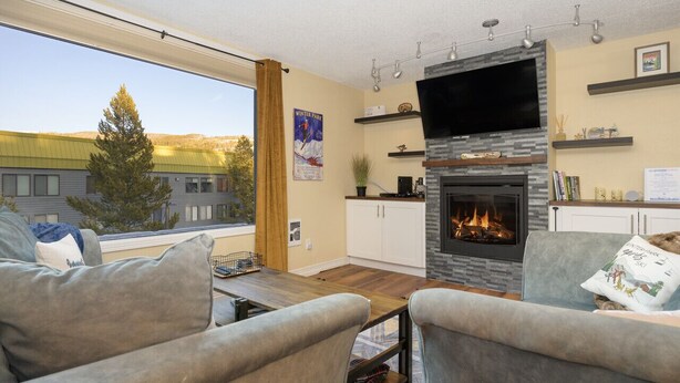 Un salon avec une cheminée, un téléviseur et une vue sur un bâtiment à l’extérieur.