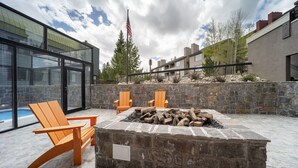 Une terrasse extérieure moderne, agrémentée d’un foyer en pierre, de deux fauteuils Adirondack en bois et d’une piscine en arrière-plan.