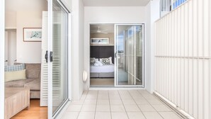 Un appartement moderne doté d’une porte-fenêtre coulissante donnant sur un balcon, d’un canapé et d’un lit avec une literie à motifs.