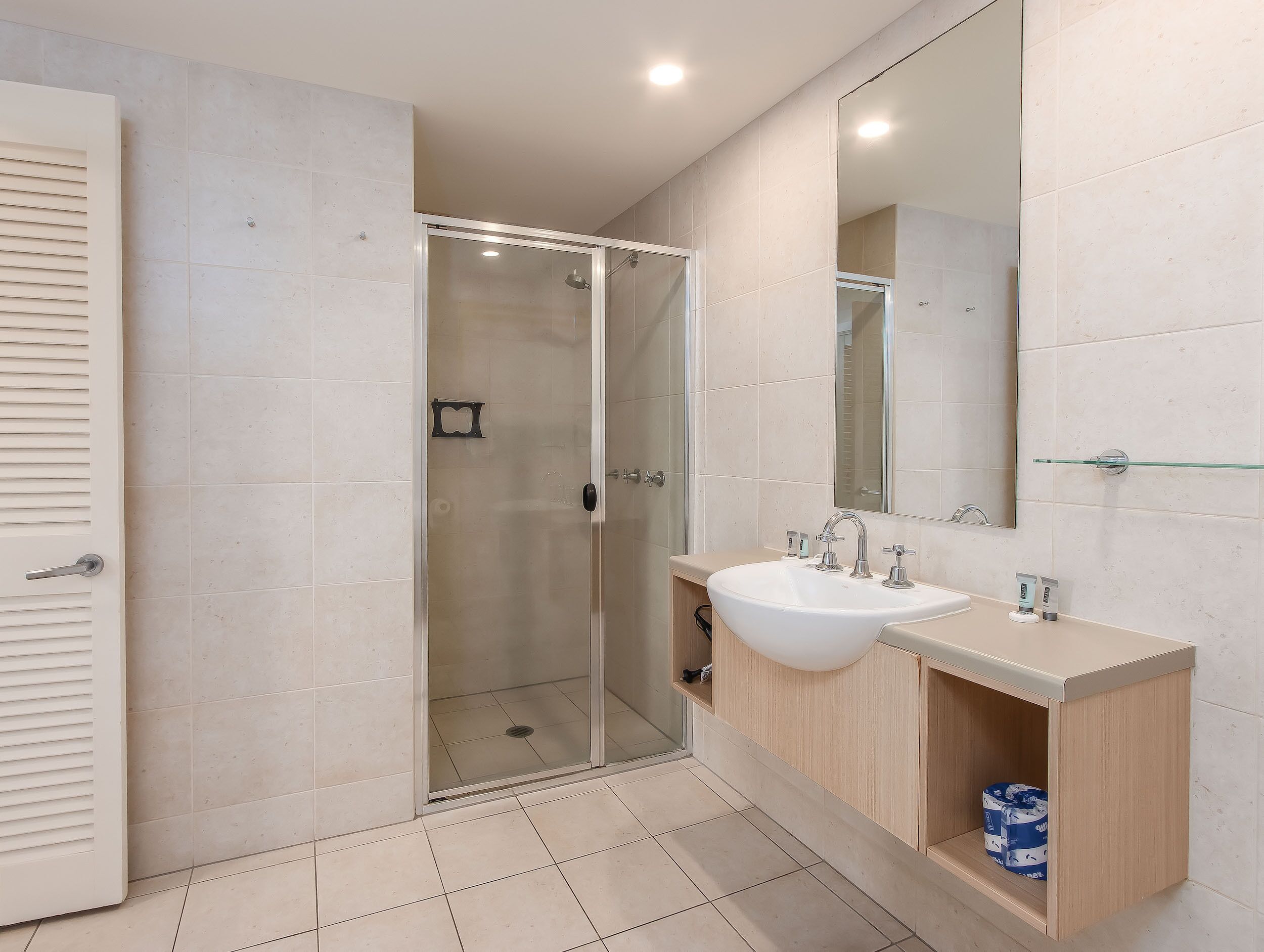 Un bagno moderno con cabina doccia in vetro, un lavandino bianco e un mobile contenitore in legno.