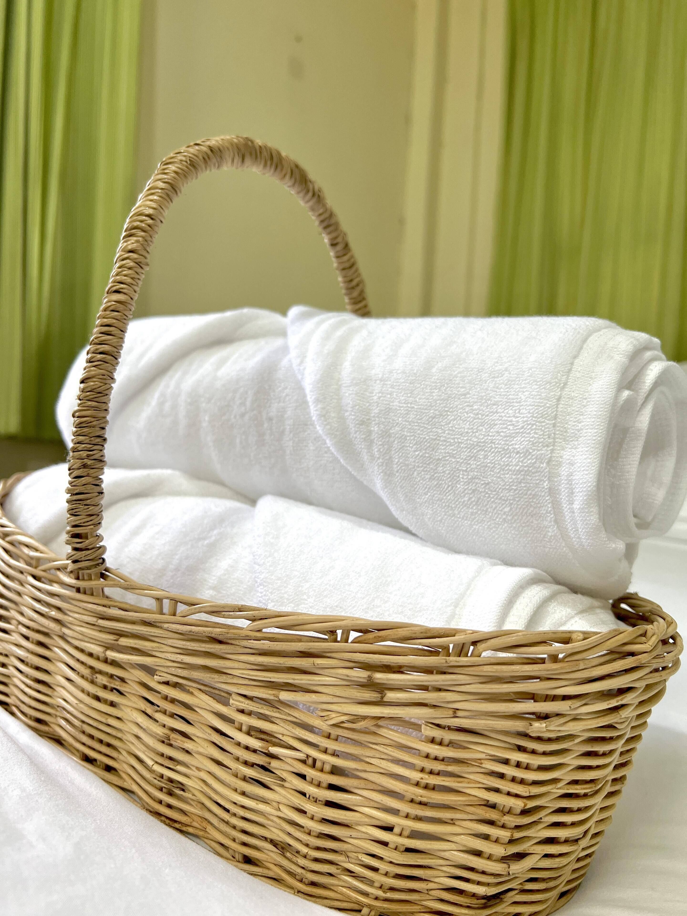 A wicker basket with a handle containing rolled white towels.