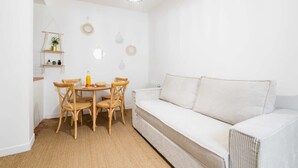 Ein weißes Zimmer mit einem runden Tisch, vier Stühlen, einer weißen Couch und einer hängenden Leuchte.