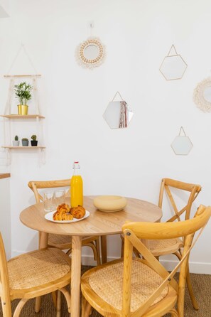 Une table de salle à manger ronde en bois, avec quatre chaises, une bouteille de jus d’orange et une assiette de croissants.