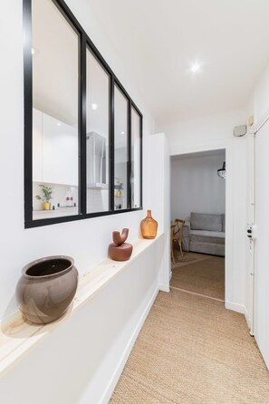 Ein Flur mit weißer Wand, einem großen Spiegel, einem Holzboden mit Dekorationen und einem grauen Sofa im Hintergrund.