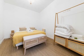 Une chambre à coucher comprenant un lit, des tables de chevet, un banc et un grand miroir.