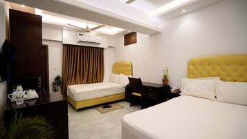A hotel room with two beds, a desk, a chair, an air conditioning unit, a ceiling fan, and a potted plant.