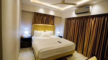 A hotel room with a large bed, two bedside tables with lamps, a ceiling fan, and an air conditioning unit.