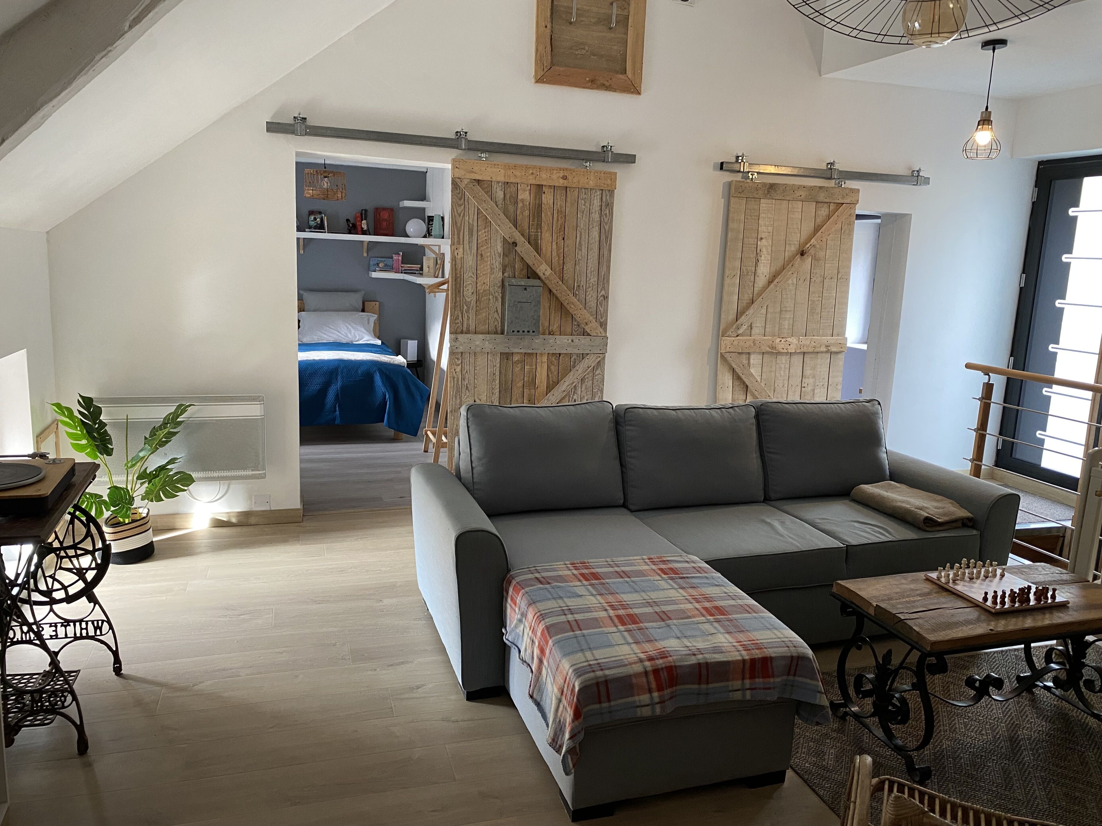 Een moderne woonkamer met een grijze bank, een geruit plaid en een schaakbord op een houten tafel.