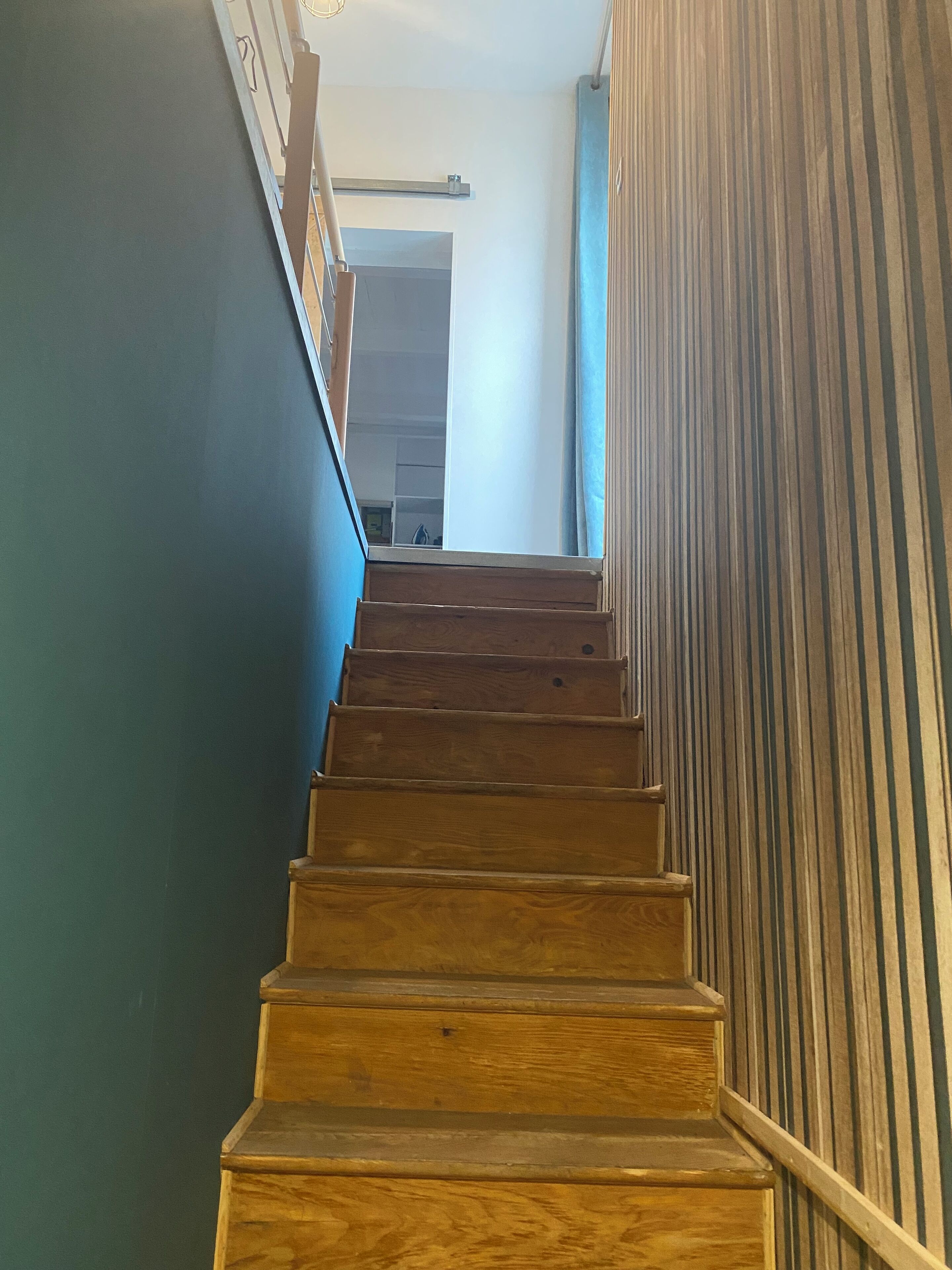 Una escalera de madera con barandilla, que conduce a una habitación con una puerta blanca y una pared azul.