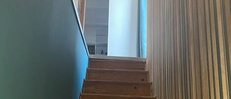 Una escalera de madera con barandilla, que conduce a una habitación con una puerta blanca y una pared azul.