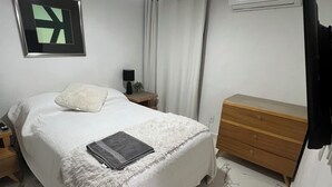 Un dormitorio con cama, mesita de noche con lámpara, cómoda, ventilador de techo y aire acondicionado.
