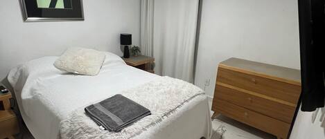 A bedroom with a bed, a bedside table with a lamp, a dresser, a ceiling fan, and an air conditioning unit.