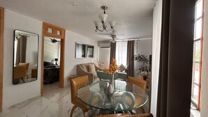 Un comedor con una mesa de vidrio rodeada de sillas de mimbre, un ventilador de techo y una araña.