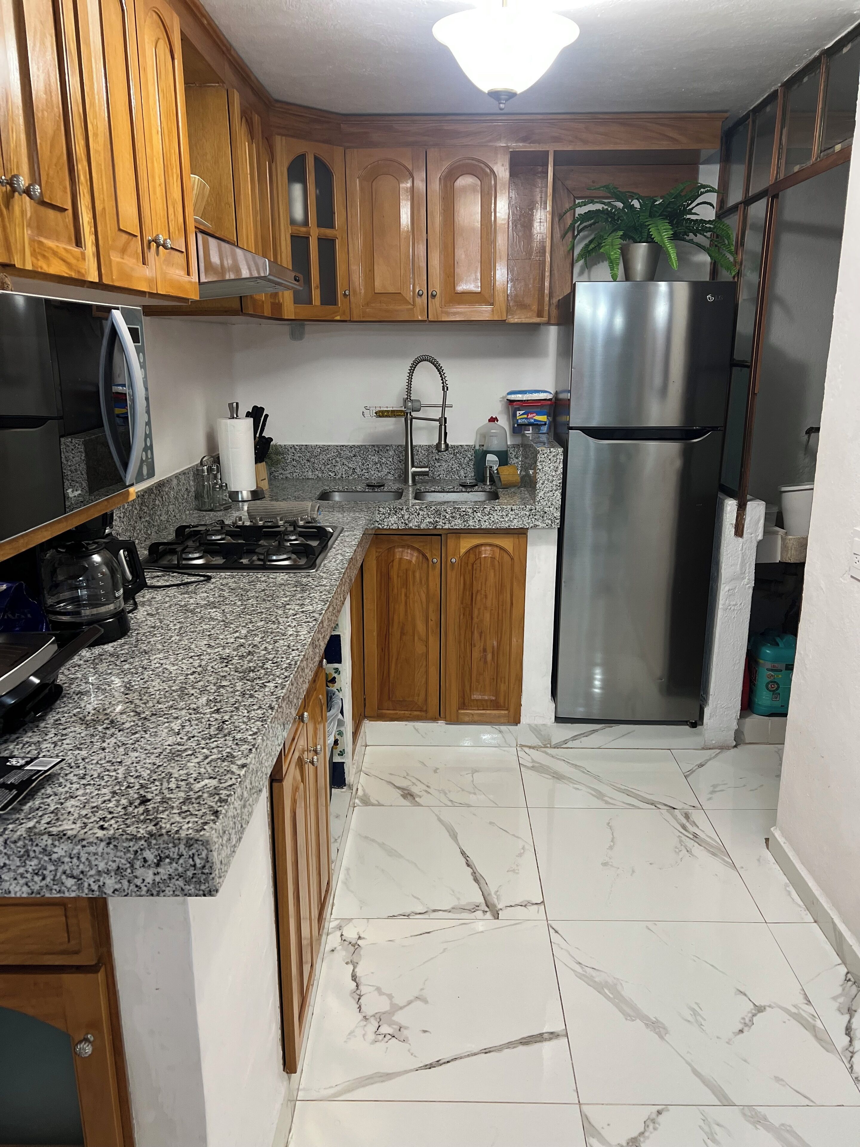 A kitchen with wooden cabinets, granite countertops, a stainless steel refrigerator, and a gas stove.