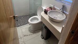 Un baño moderno con ducha de vidrio, inodoro blanco, piso de mármol y lavamanos.