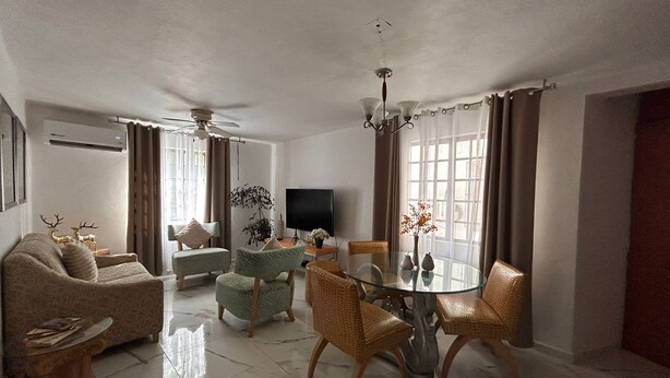 Una sala de estar con un sofá, sillones, una mesa de comedor de vidrio y un televisor.