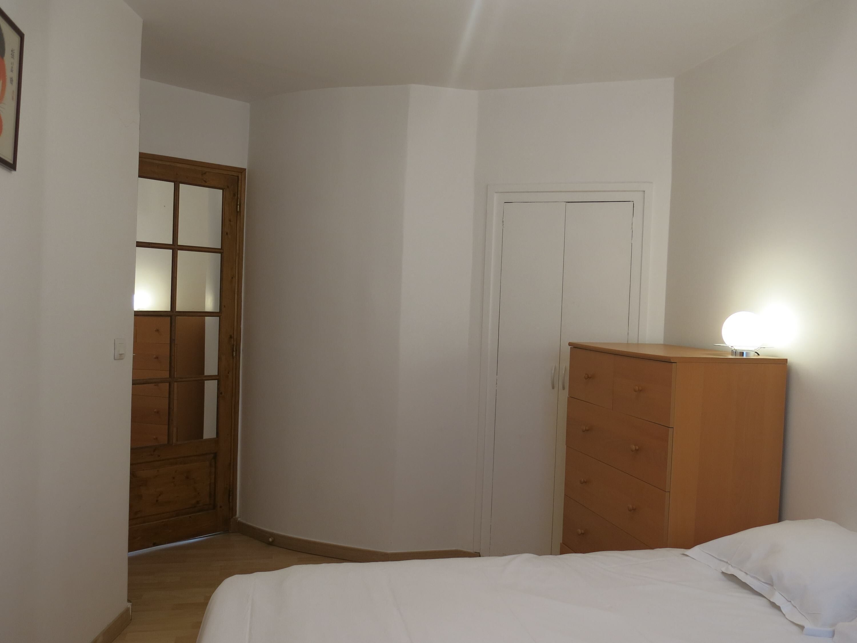 Ein Schlafzimmer mit einem Holzschrank, einem Bett mit weißer Bettwäsche und einer Tür mit Milchglasfenster.