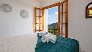 A bedroom with a bed, a view through open windows, and a balcony.