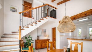 A spacious dining area with a wooden table, chairs, and a bottle of wine. A staircase with wooden railings leads to an upper level.