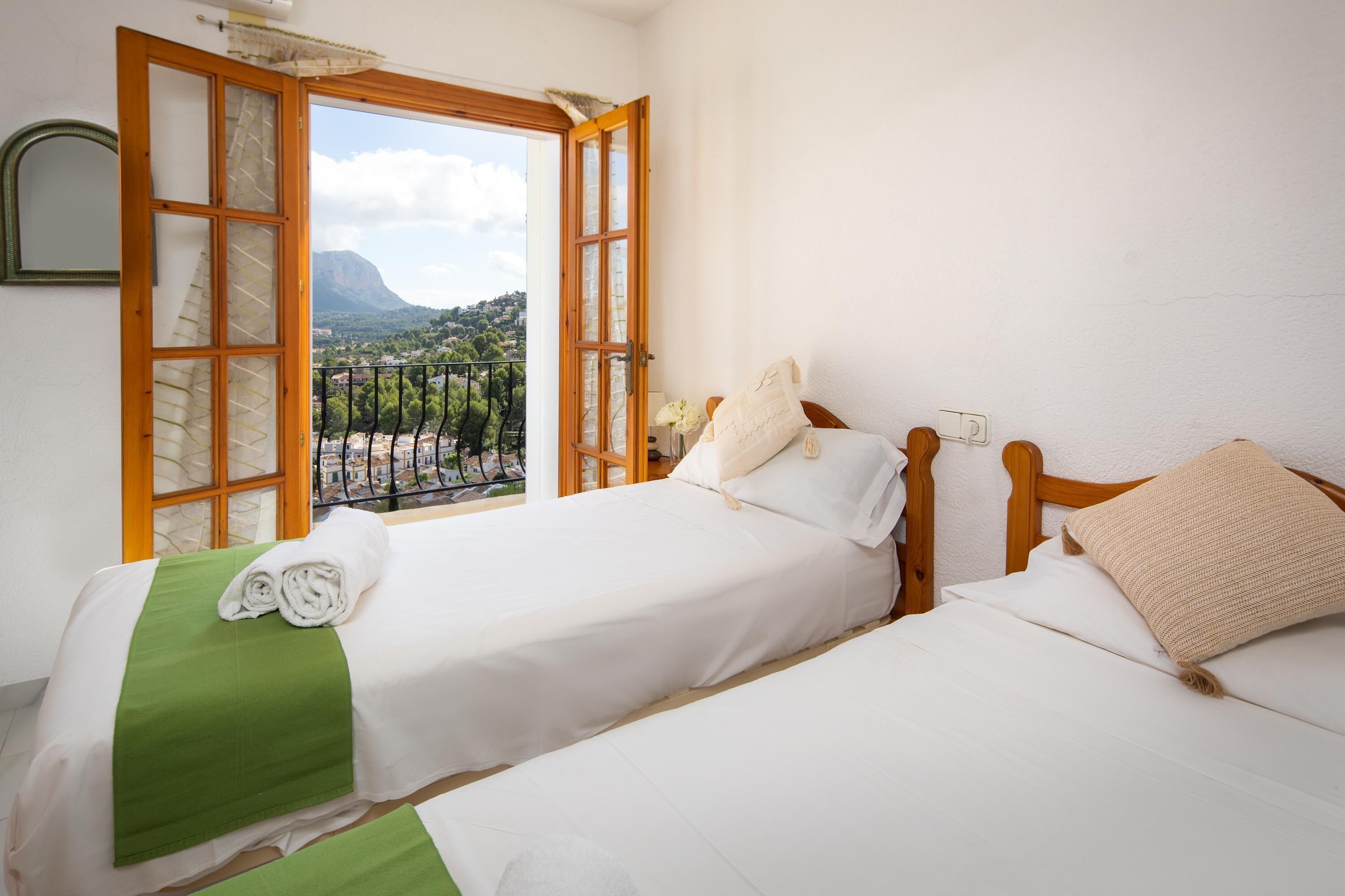 Habitación de hotel con dos camas, balcón y vista a la montaña.