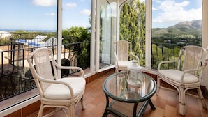 A balcony with wicker chairs and a glass table, offering a view of a mountainous landscape.