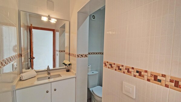 A bathroom with a sink, mirror, toilet, and a towel on the counter.