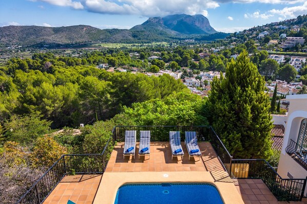 Una piscina en la azotea con sillones de descanso y vistas a un pueblo y montañas.