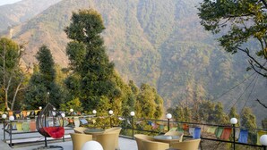 An outdoor seating area with wicker furniture and a hanging chair, overlooking a mountainous landscape. - Dharamshala Village Resort (Dharamshala)
