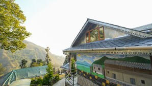 A house with a sloped roof, a mural on the side, and a view of a mountain. - Dharamshala Village Resort (Dharamshala)