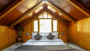A bedroom with a wooden ceiling, a large bed with white bedding, two nightstands, a potted plant, and a window with a view. - Dharamshala Village Resort (Dharamshala)