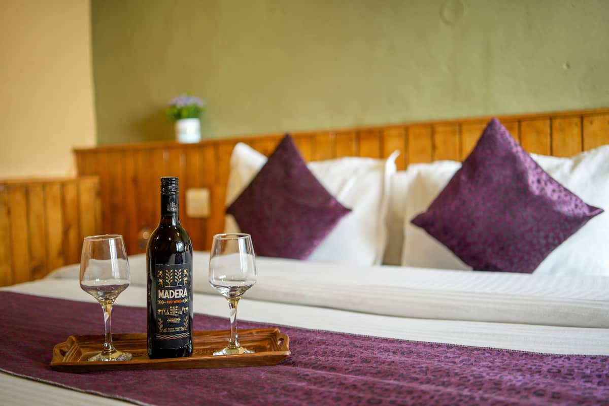 Uma cama com cabeceira de madeira, duas almofadas roxas e uma garrafa de vinho tinto sobre um tabuleiro.